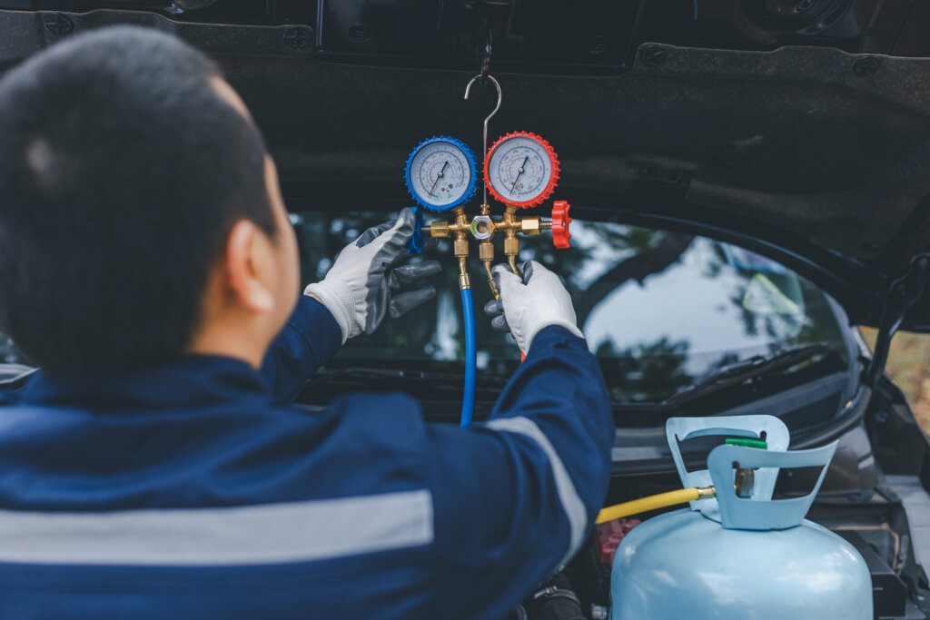 Ein Mann überprüft bei geöffneter Motorhaube die Klimaanlage eines Autos und befüllt sie mit Kältemittel.